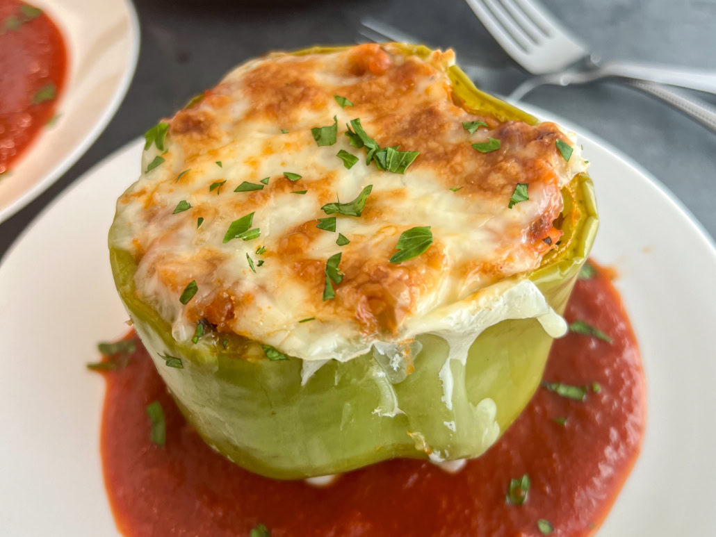 A green bell pepper stuffed with filling, topped with melted cheese and herbs, served on a plate with tomato sauce.