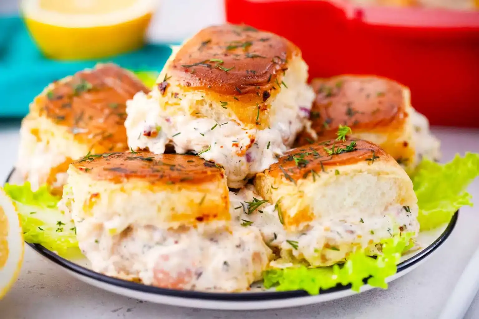 A plate of baked sliders with a creamy chicken filling, garnished with herbs, served on a bed of lettuce.