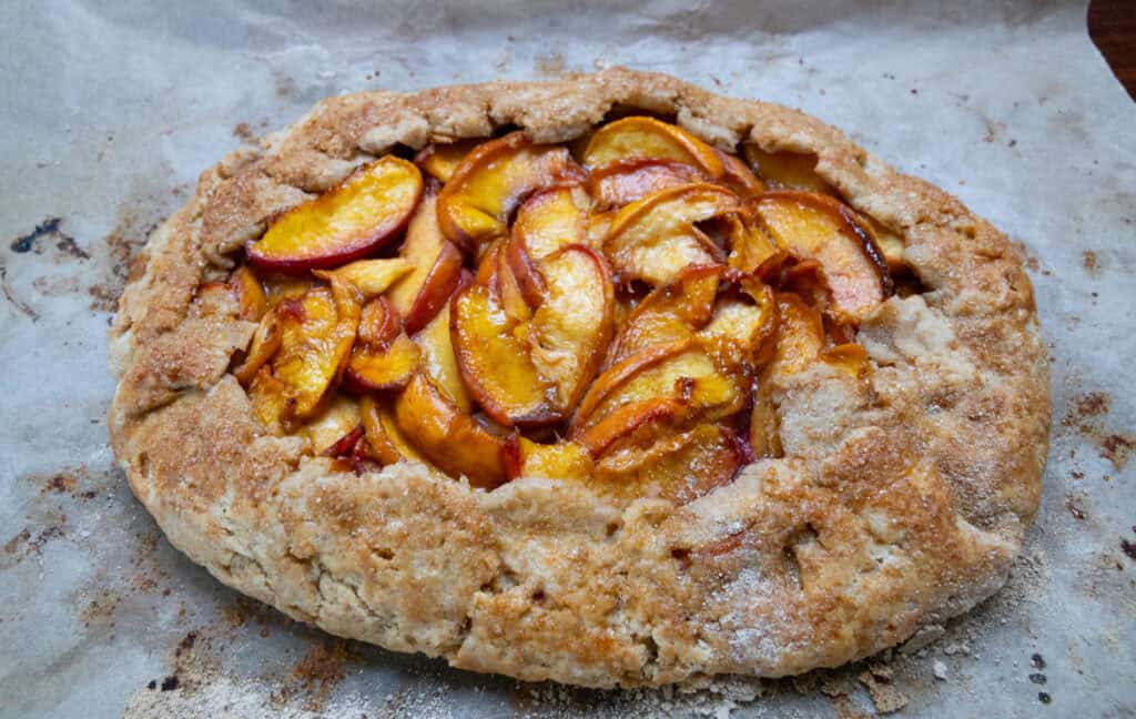A rustic peach galette with a golden, flaky crust and sliced peaches, baked on parchment paper.