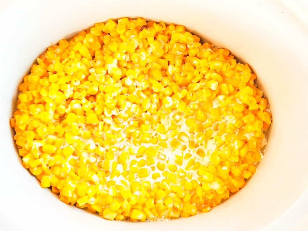 A slow cooker filled with yellow corn kernels and cream.