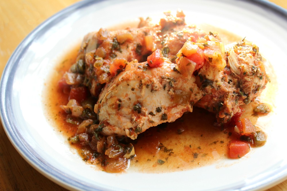 A plate of cooked chicken breast topped with a tomato-based sauce containing chopped vegetables and herbs.