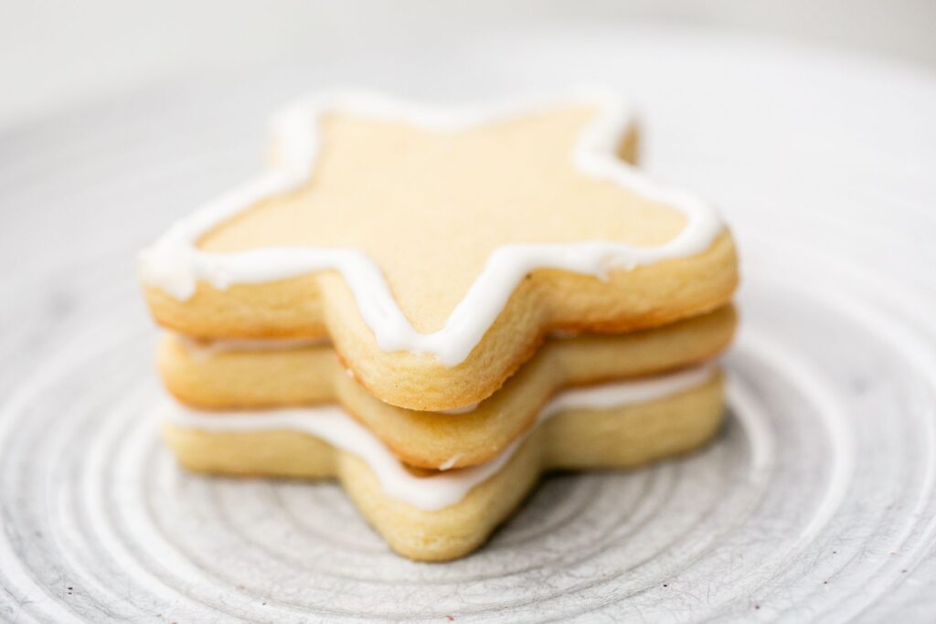 Three star-shaped sugar cookies with white icing stacked on a light, textured plate.