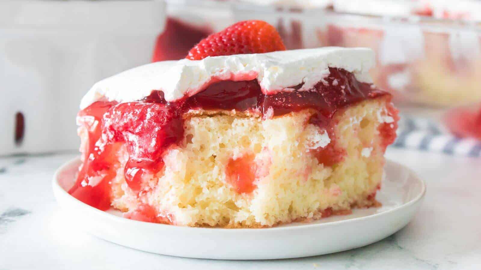 A slice of strawberry poke cake with whipped cream topping and strawberry glaze, served on a white plate.