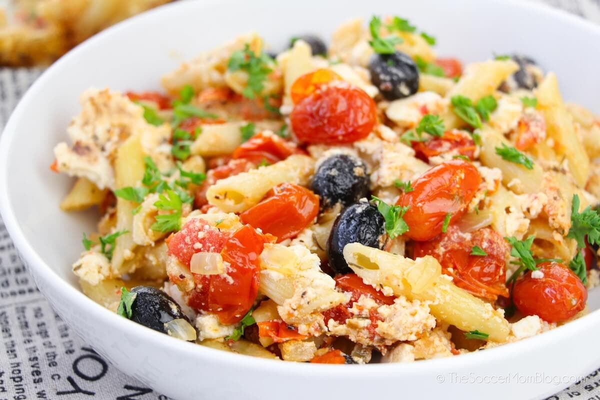 A bowl of pasta with tomatoes and olives.