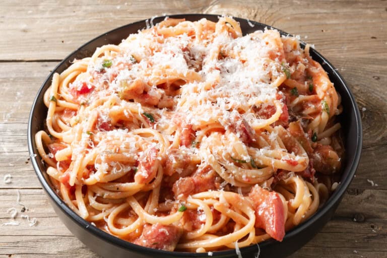 A bowl of spaghetti topped with tomato sauce, diced tomatoes, herbs, and grated cheese, placed on a wooden surface.