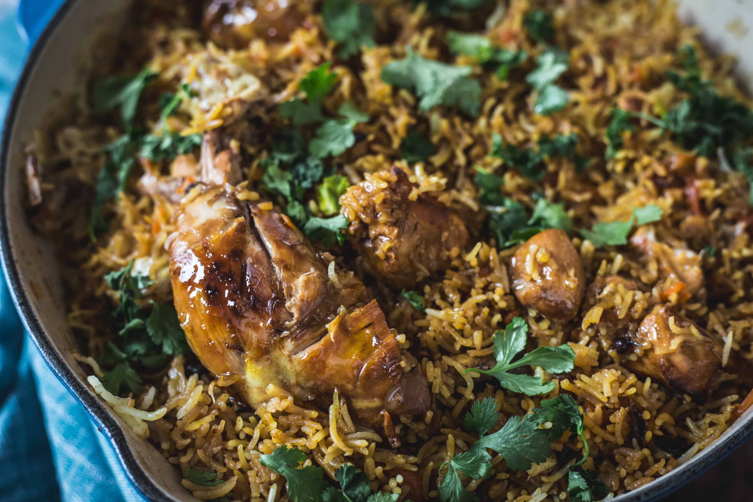 A close-up of cooked biryani rice with pieces of chicken and garnished with fresh cilantro.