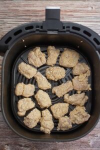 Raw breaded chicken pieces arranged in a single layer inside an air fryer basket on a wooden surface.