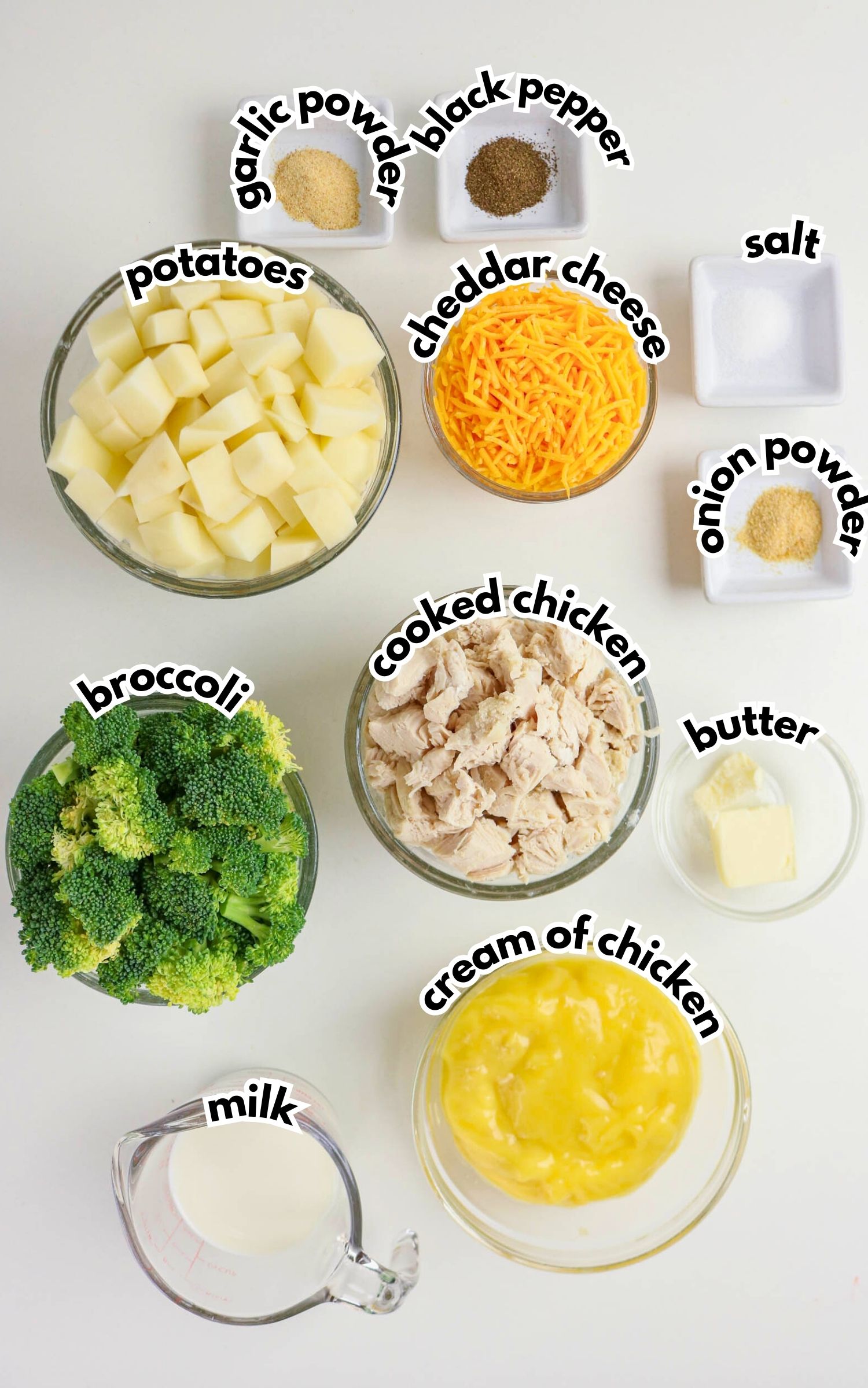 Bowls of chopped potatoes, broccoli, cooked chicken, shredded cheddar cheese, cream of chicken soup, butter, milk, and small dishes of garlic powder, black pepper, salt, and onion powder.