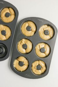Two donut pans filled with raw coffee doughnut batter, ready to be baked, are placed on a white surface.