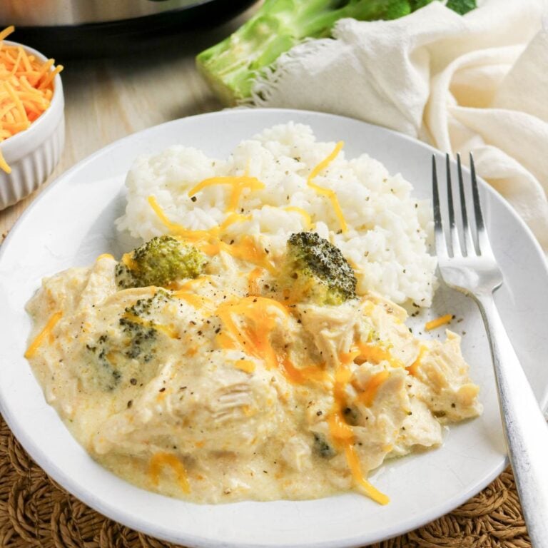 A plate of white rice served with creamy chicken, broccoli, and shredded cheddar cheese, with a fork on the side.