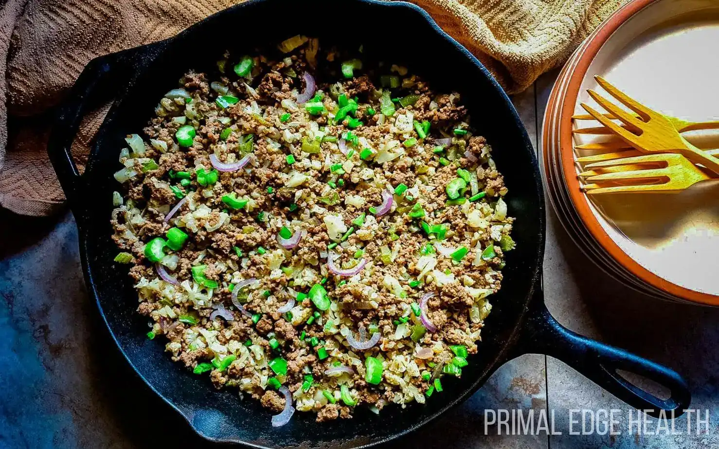 A skillet filled with cooked ground beef, green peas, chopped vegetables, and sliced onions, with a fork and plate nearby.
