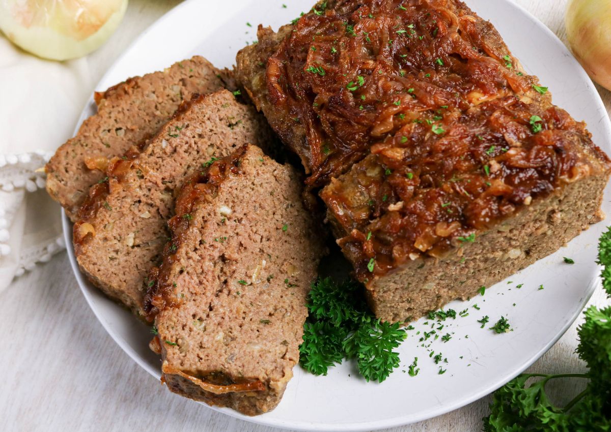 Sliced meatloaf with a caramelized onion topping is arranged on a white plate, garnished with parsley.