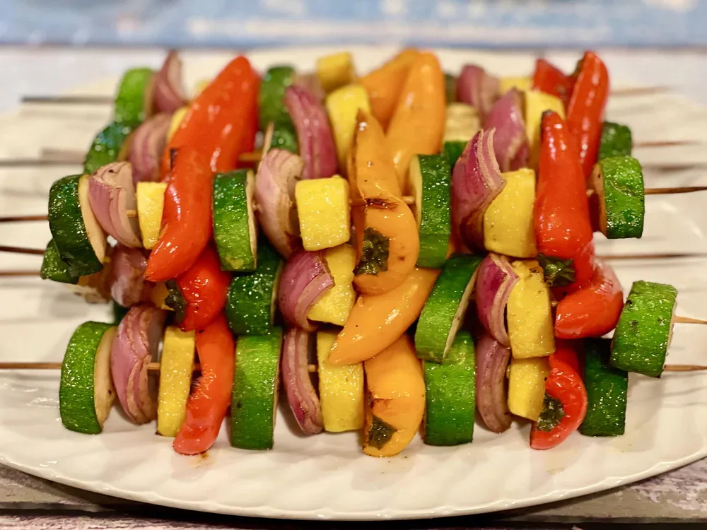 Skewers of sliced zucchini, yellow squash, red onion, and bell peppers arranged on a white plate.