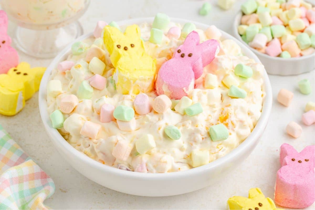 A white bowl filled with creamy marshmallow salad, topped with colorful mini marshmallows and yellow and pink marshmallow bunny candies.