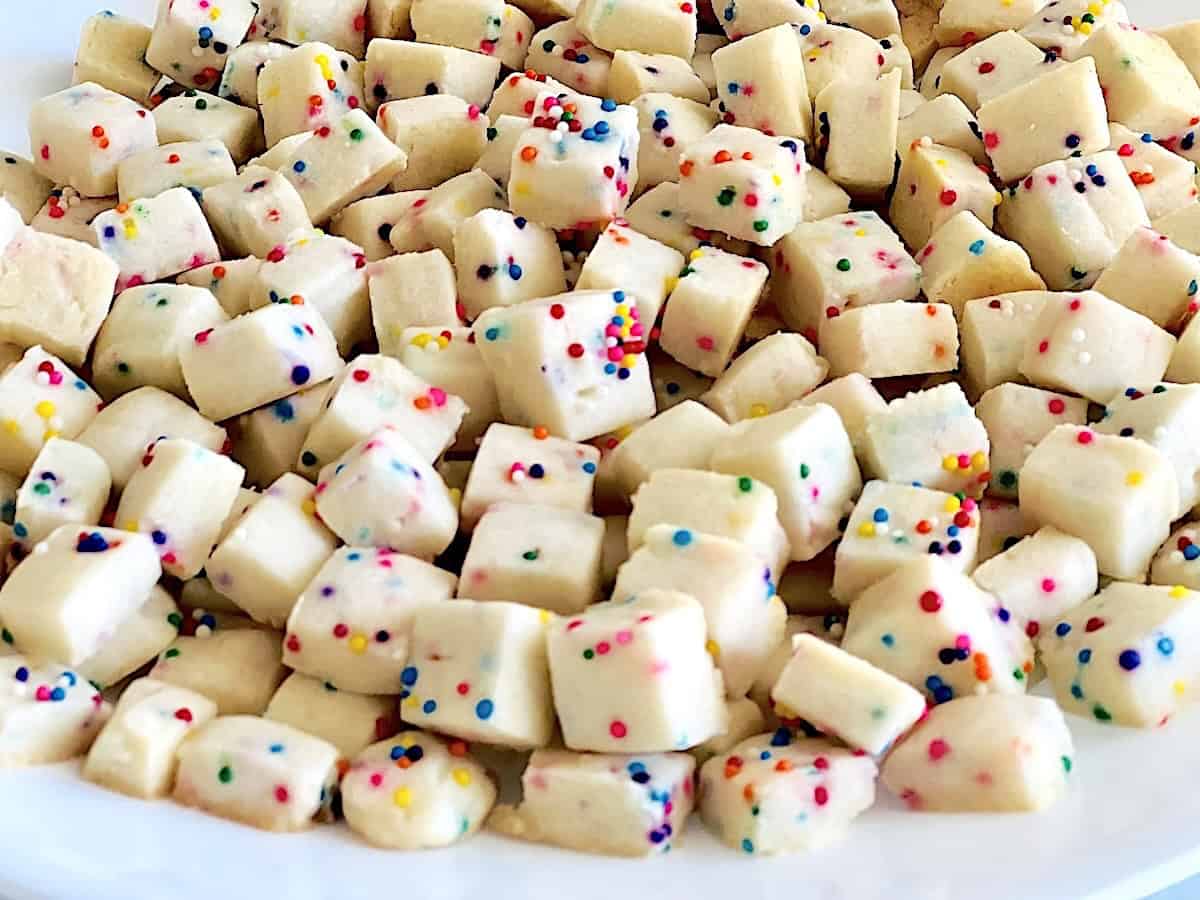 Small square shortbread cookies with colorful sprinkles scattered on a white plate.
