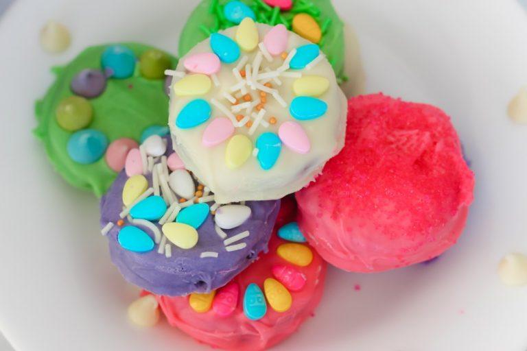 Colorful decorated cookies with various pastel icing and sprinkles are arranged on a white plate.