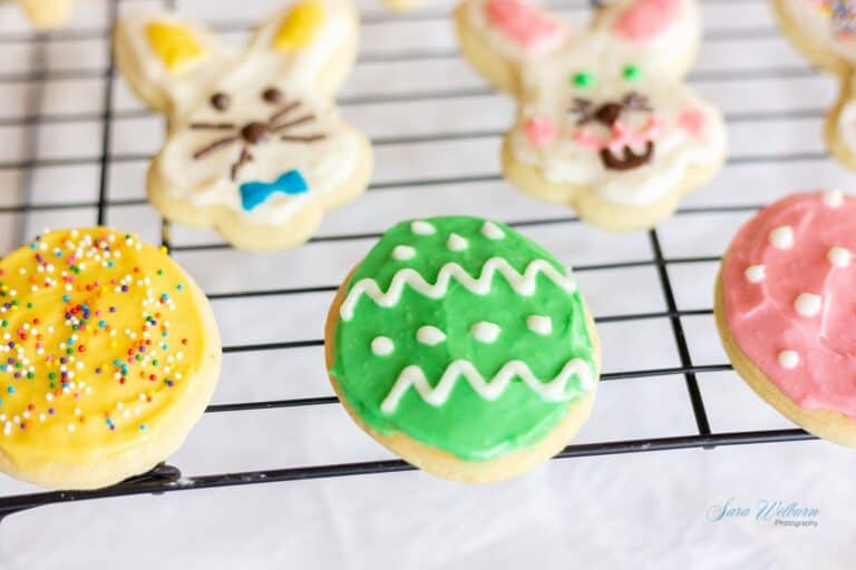 Colorful Easter cookies, including egg-shaped cookies with icing and sprinkles, and bunny-shaped cookies, displayed on a cooling rack.