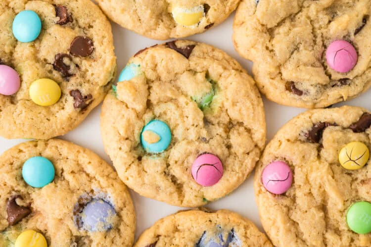 Close-up of several cookies with colorful candy-coated chocolates and chocolate chips on a white surface.