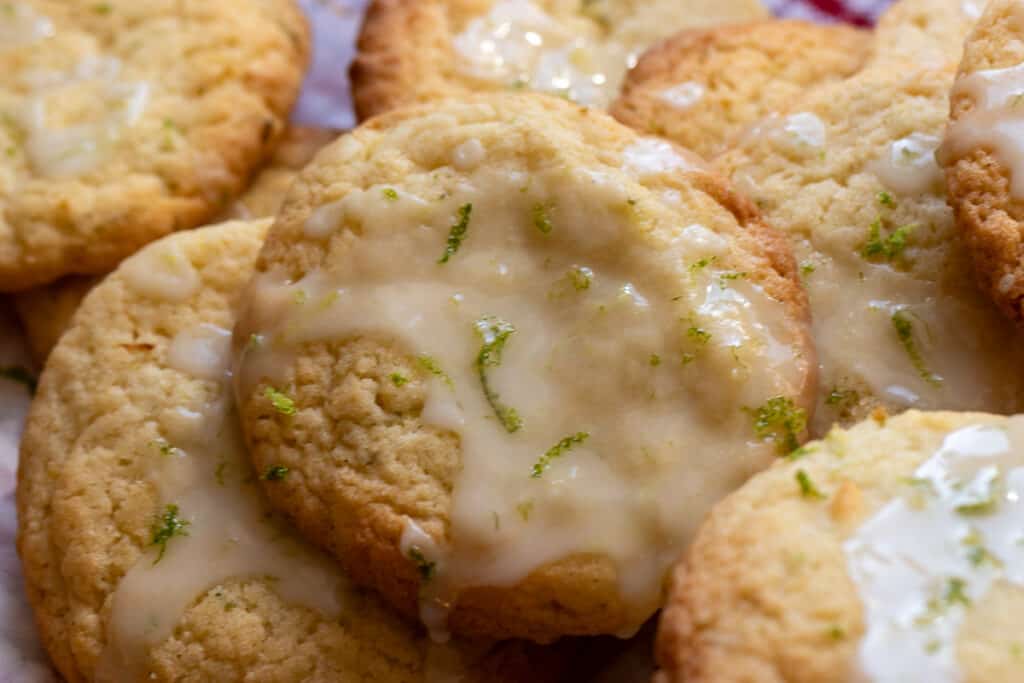 Close-up of glazed cookies with lime zest on top, stacked together on a surface.