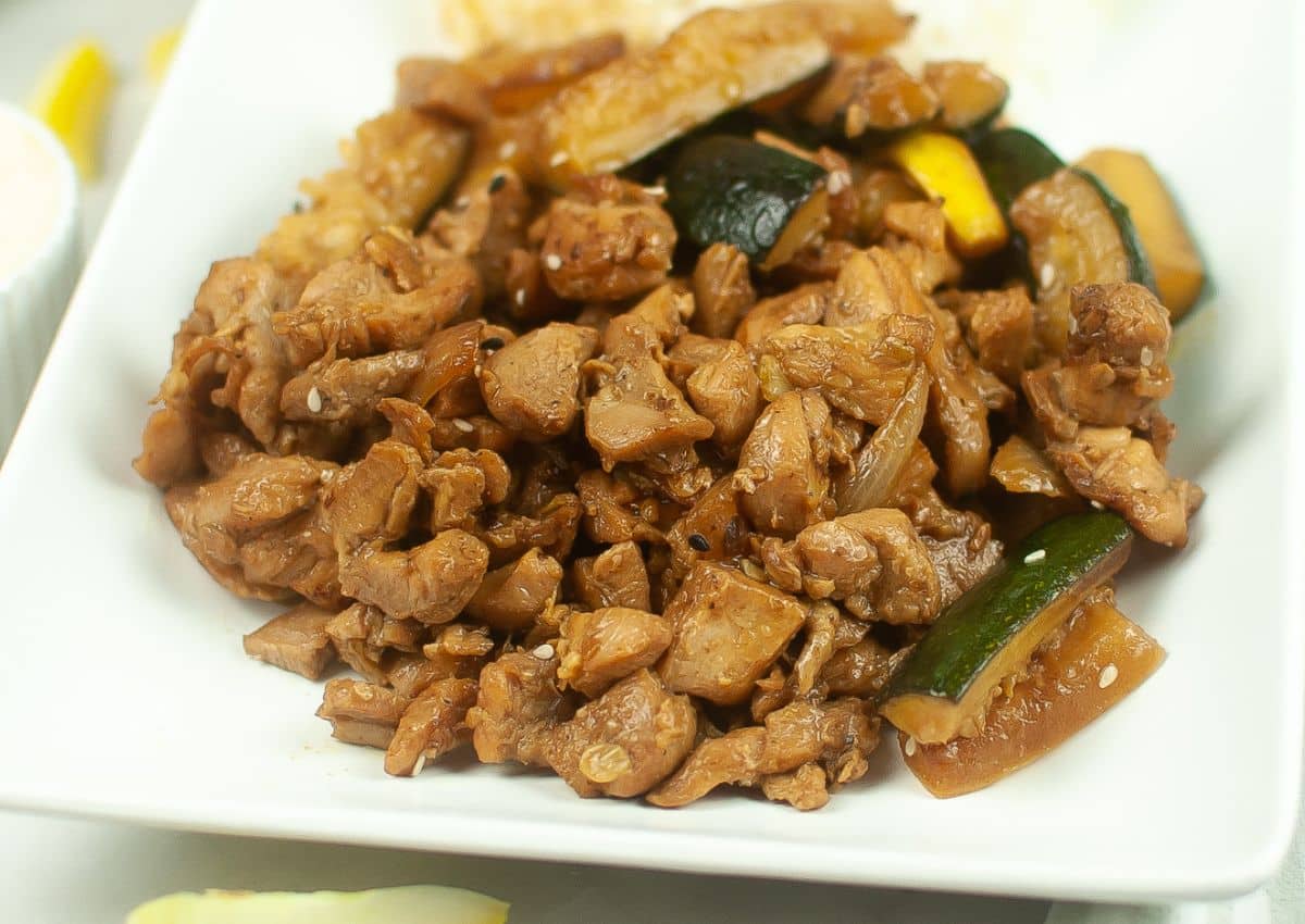 A plate of stir-fried chicken with zucchini and onions, served on a white dish.