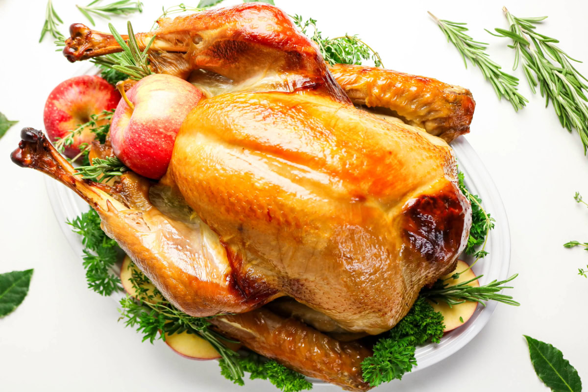 A whole roasted turkey garnished with fresh herbs and apples is presented on a white platter.