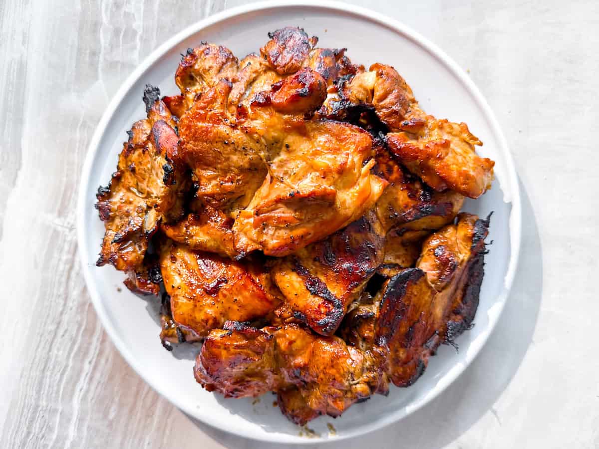 Plate of grilled, marinated chicken pieces with a charred, golden-brown exterior on a white plate, viewed from above.