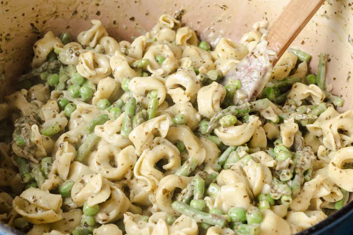 A bowl of pasta with green peas and asparagus.