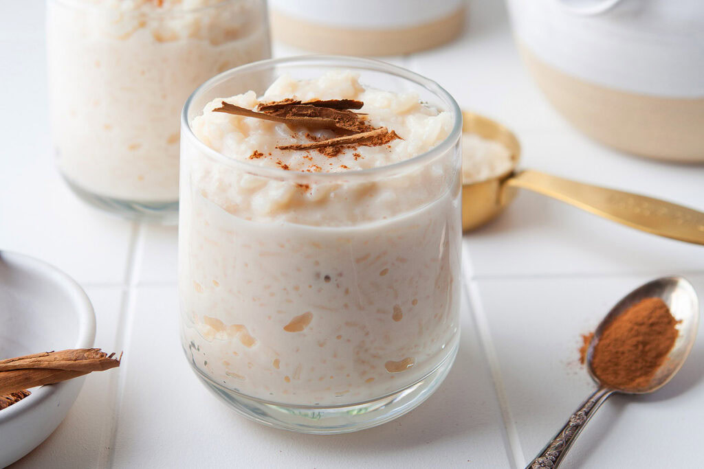 A glass of rice pudding with cinnamon sticks.
