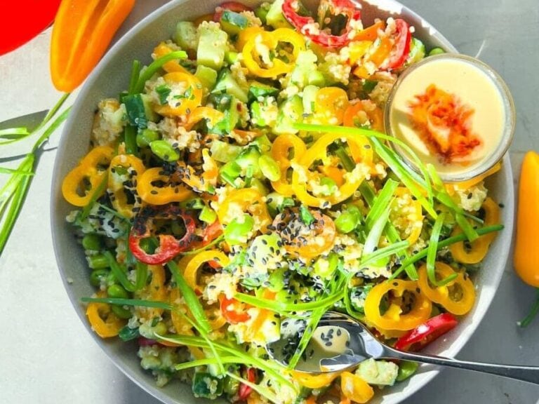 A colorful salad with sliced mini bell peppers, greens, black sesame seeds, and a small bowl of creamy dressing on the side.