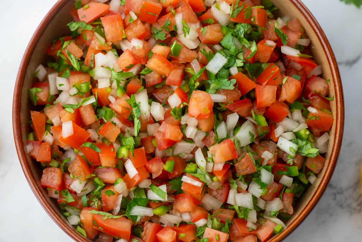 A bowl filled with freshly chopped pico de gallo made of tomatoes, onions, cilantro, and green peppers.