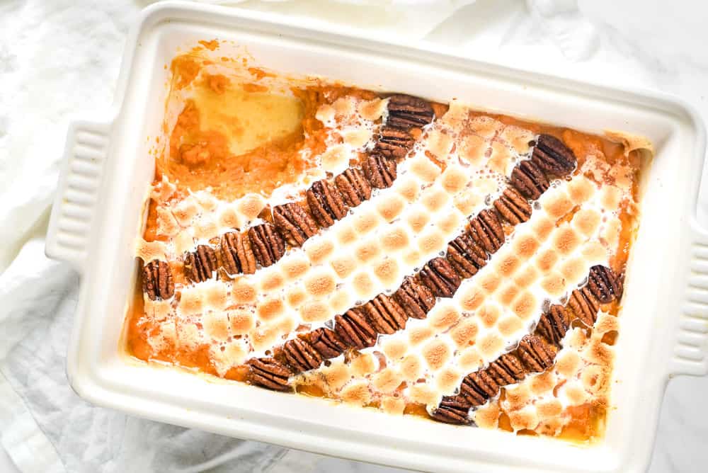 Rectangular baking dish filled with sweet potato casserole topped with toasted marshmallows and rows of pecan halves, with a portion missing from the top left corner.