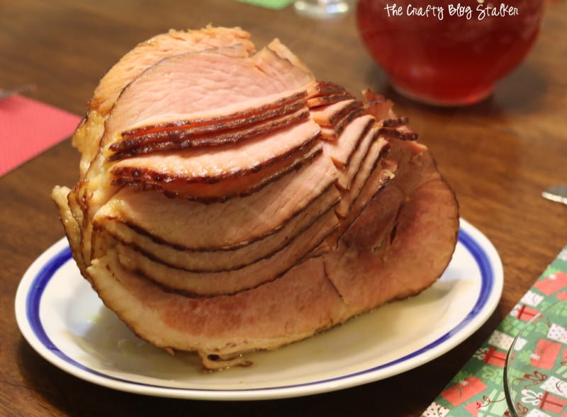 A spiral-sliced ham is served on a white plate with a blue rim, placed on a wooden table with holiday-themed napkins.