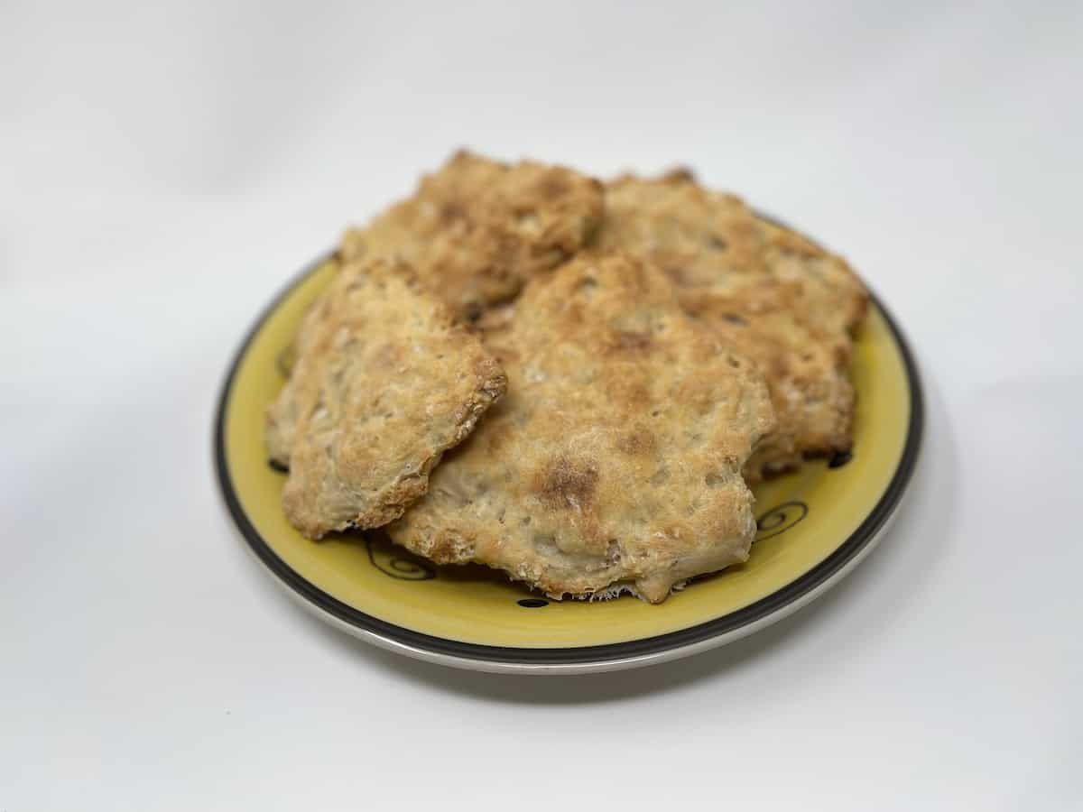 A yellow plate with several pieces of homemade, irregularly shaped, baked bread or biscuits on a white background.