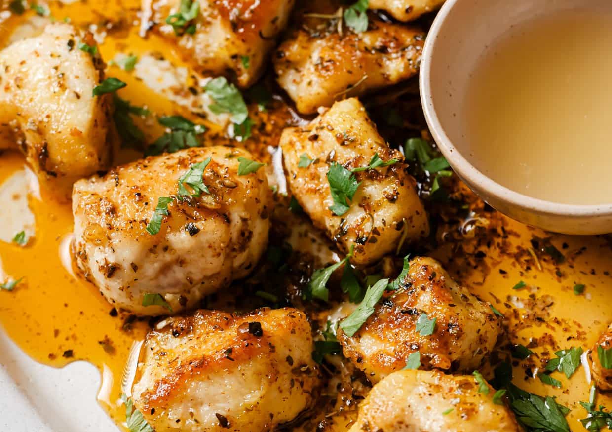 Close-up of seasoned, cooked chicken pieces garnished with chopped herbs, served with a small bowl of sauce on the side.