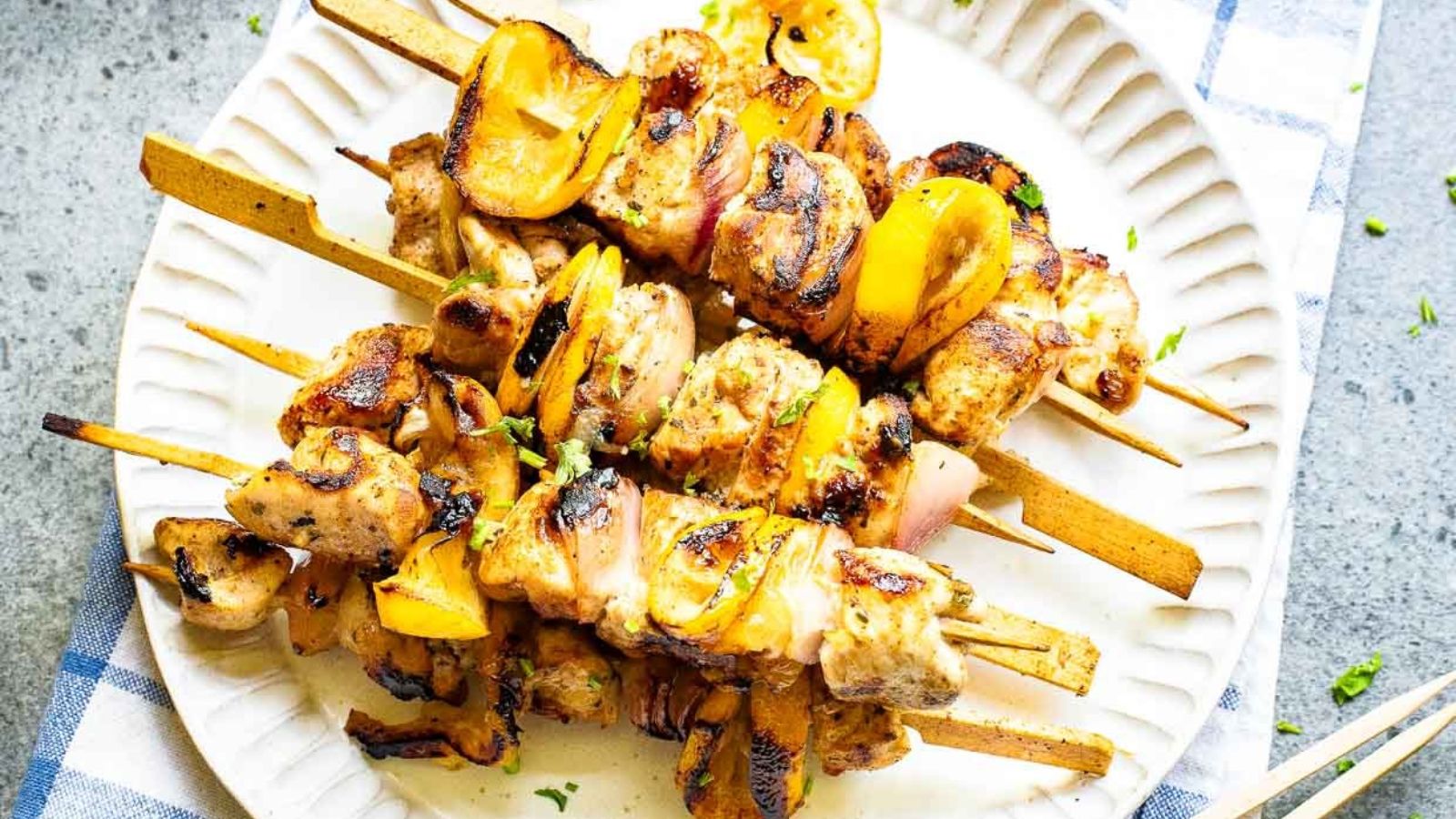 Grilled chicken and vegetable skewers arranged on a white plate, with visible char marks and a few herbs sprinkled on top.