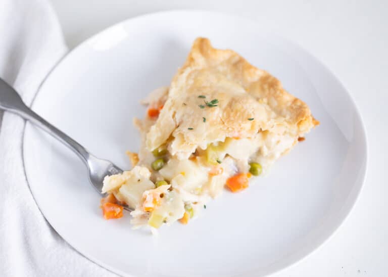 A slice of vegetable pot pie with a flaky crust on a white plate, with a fork taking a bite.