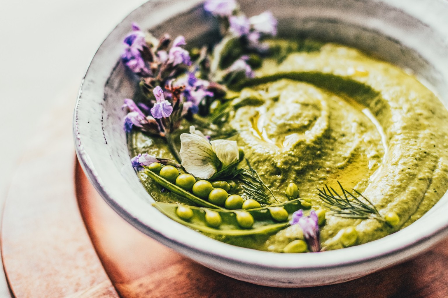 A bowl of green pea hummus garnished with fresh peas, edible flowers, and herbs.