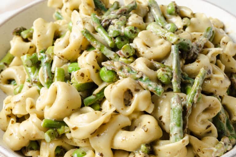 A close-up of tortellini pasta mixed with asparagus, green peas, and a herb sauce.
