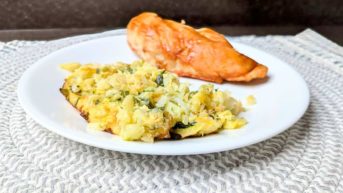 A white plate with a serving of baked chicken breast and a portion of cabbage casserole on a woven placemat.