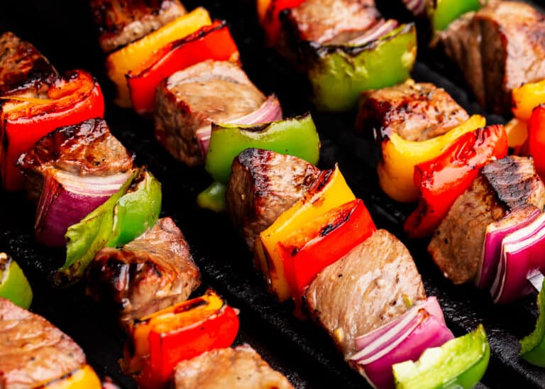 Close-up of grilled beef kebabs with chunks of red and green bell peppers, yellow bell peppers, and red onion on skewers.