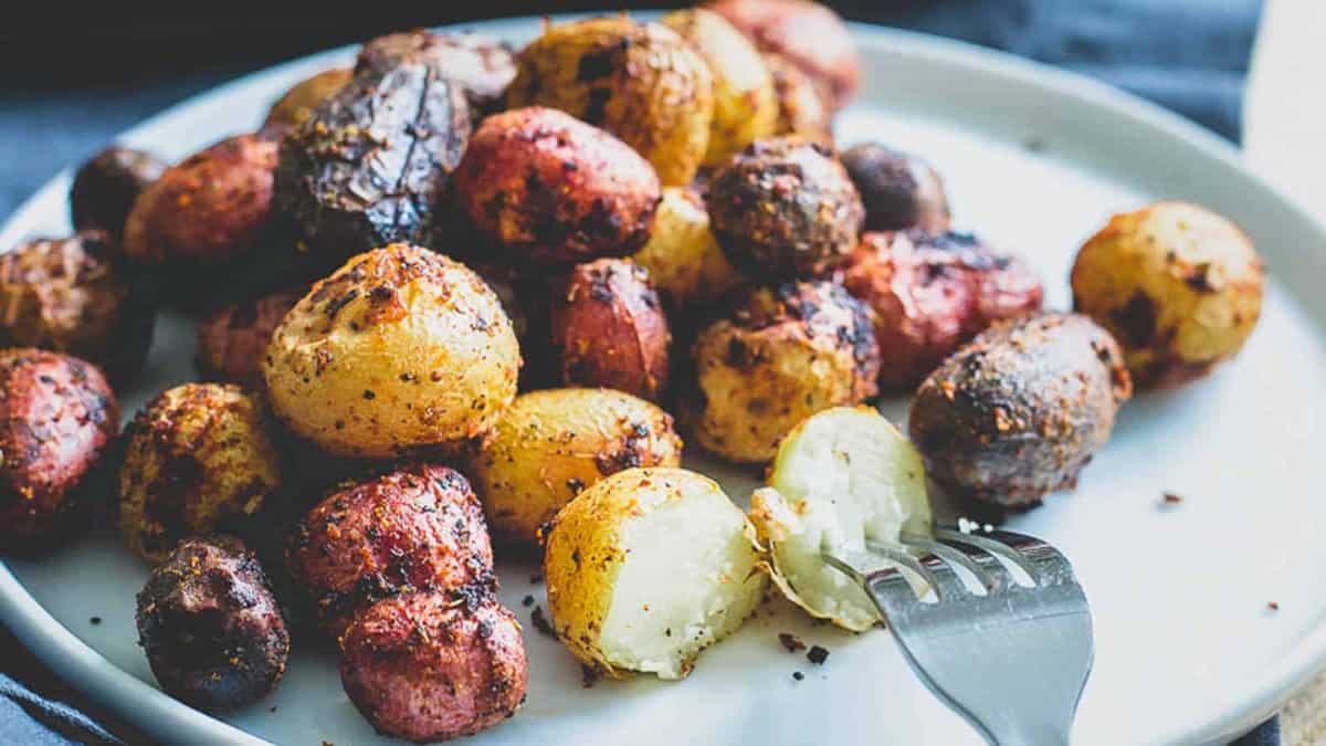 A plate of assorted roasted baby potatoes, some halved with a fork, showing crispy, browned skin and a soft interior.