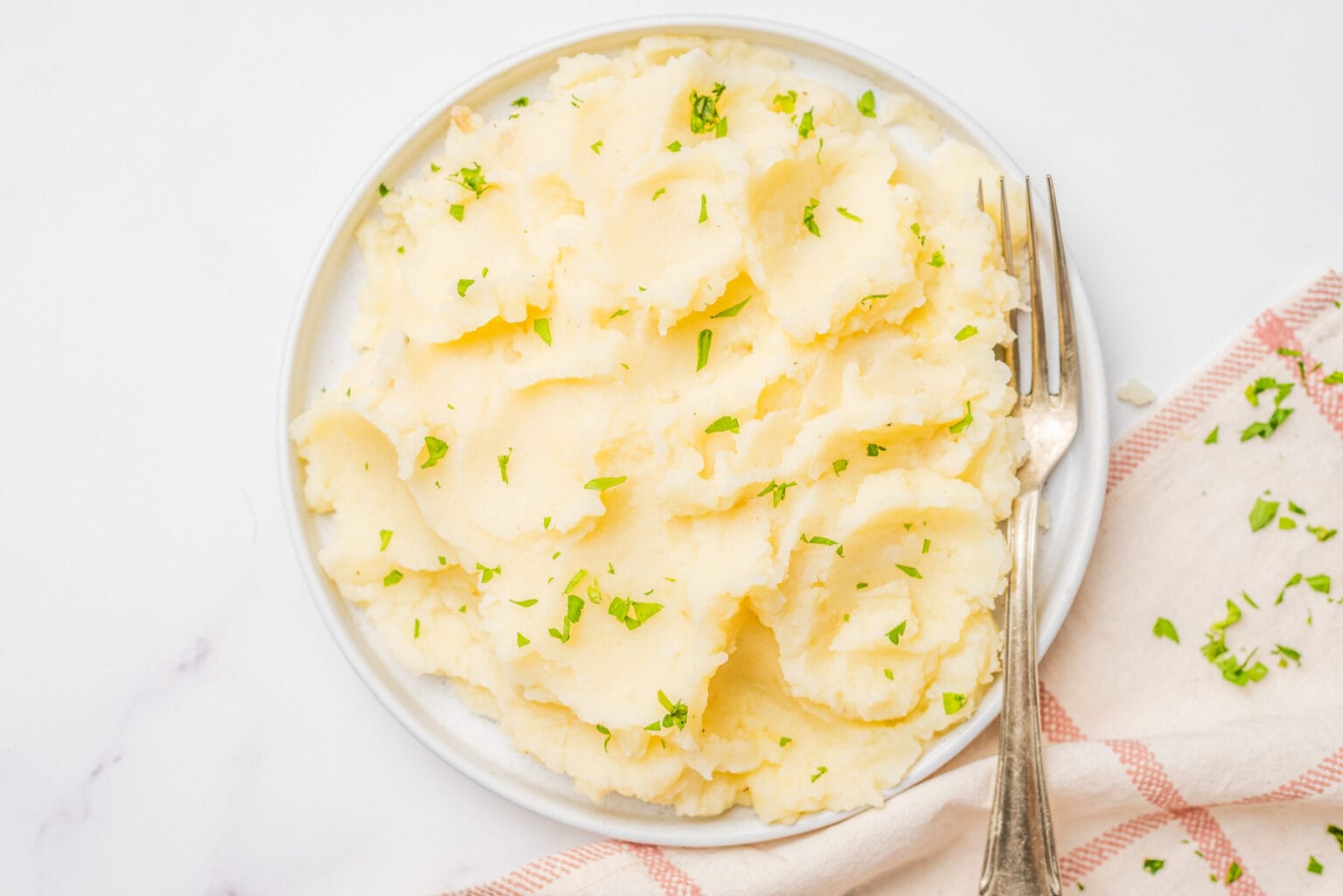 A plate of mashed potatoes garnished with chopped herbs, served with a fork on the side and a napkin partially visible.