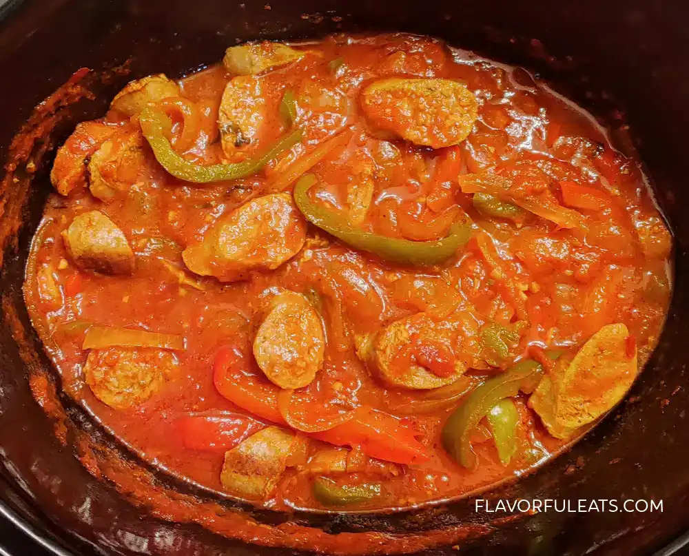 Sliced sausages with green and red bell peppers in a thick tomato-based sauce inside a slow cooker.