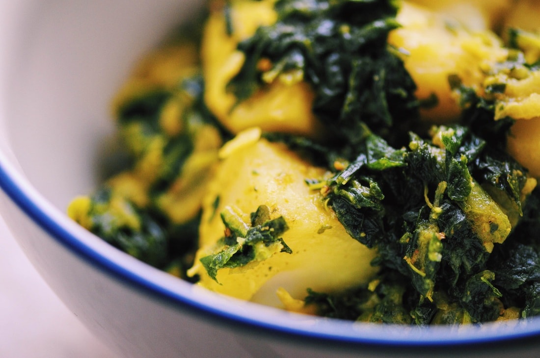 Close-up of a bowl containing cooked potatoes mixed with leafy greens and spices.