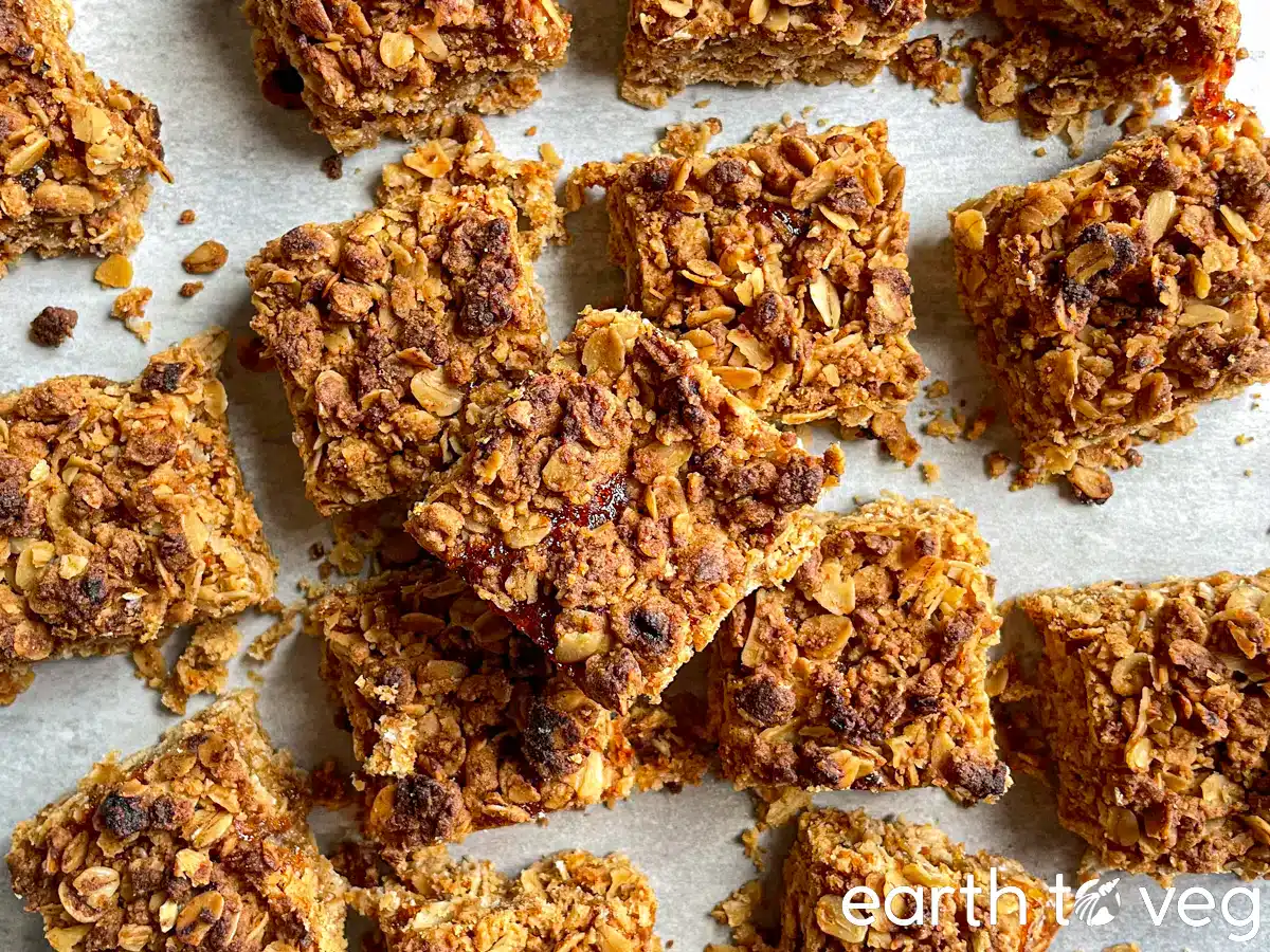 Granola bars cut into squares and arranged on parchment paper, showing a crumbly oat texture. The words earth to veg appear in the bottom right corner.