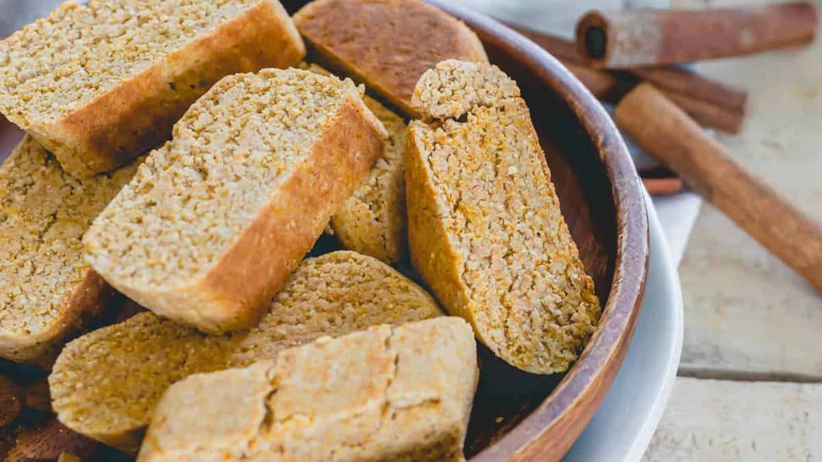 A wooden bowl filled with pieces of cornbread biscotti, with whole cinnamon sticks placed beside the bowl.