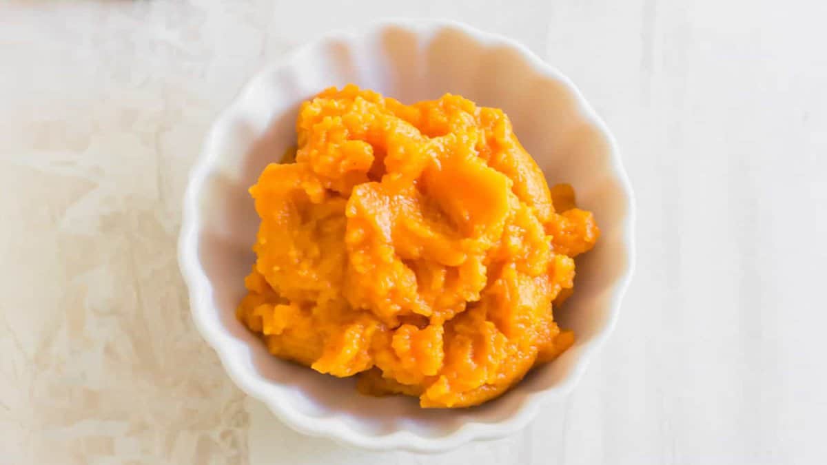 A small white bowl filled with smooth orange sweet potato mash, placed on a light-colored surface.
