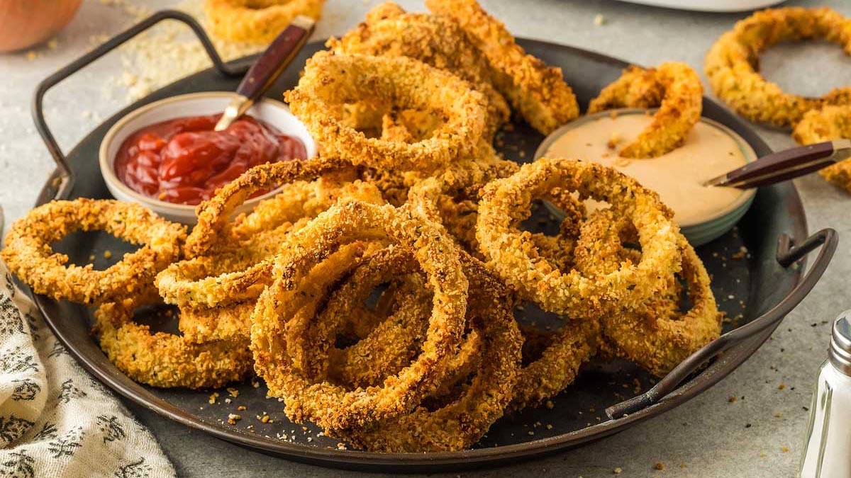 A plate of crispy baked onion rings served with bowls of ketchup and a creamy dipping sauce.