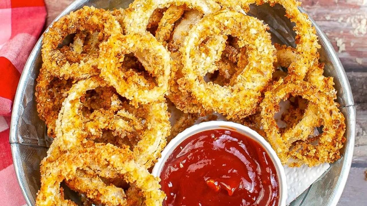 A basket of crispy, breaded onion rings served with a small dish of ketchup on the side.