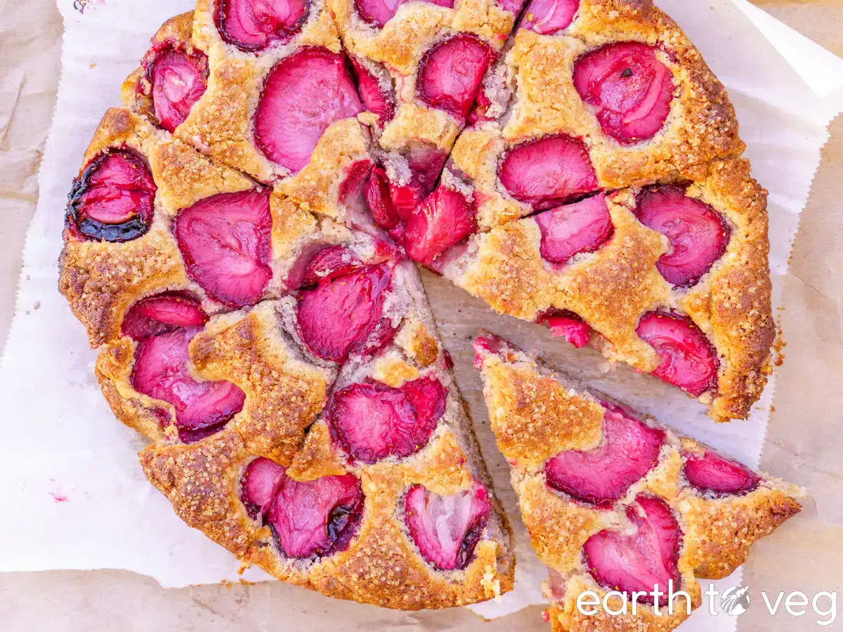 A sliced strawberry cake with a golden-brown crust sits on parchment paper, showing vibrant red strawberries on top.